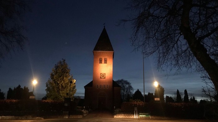 En mørk nattehavn med en lyset murstenet kirke med tårn og klokke.