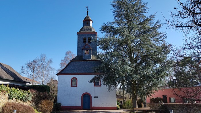 Idyllische weiße Kirche mit Glockenturm in einer ruhigen, landschaftlich gestalteten Dorfgegend.