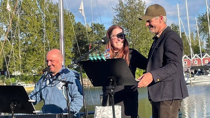 Udendørs musikalsk optræden med pianist, sanger og vært ved en naturskøn havnefront, der promoverer *