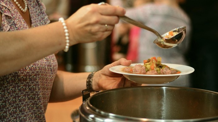 Eine Frau bedient sich bei einem Buffet und holt sich Essen mit einer Schöpfkelle auf ihren Teller.