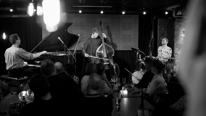 Intim jazzoptræden med et liveband, der spiller for et opmærksomt publikum i en hyggelig lokalitet.