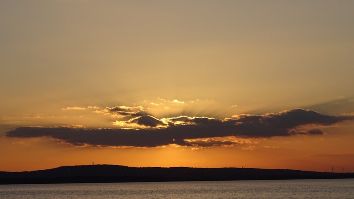 Ein ruhiger Sonnenuntergang über einem Gewässer mit Wolken und Horizont.