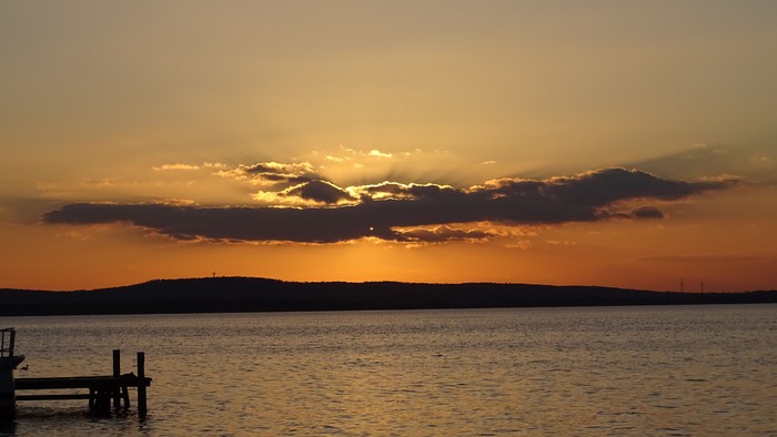 Ein ruhiger Sonnenuntergang über einem Gewässer mit Wolken und Horizont.