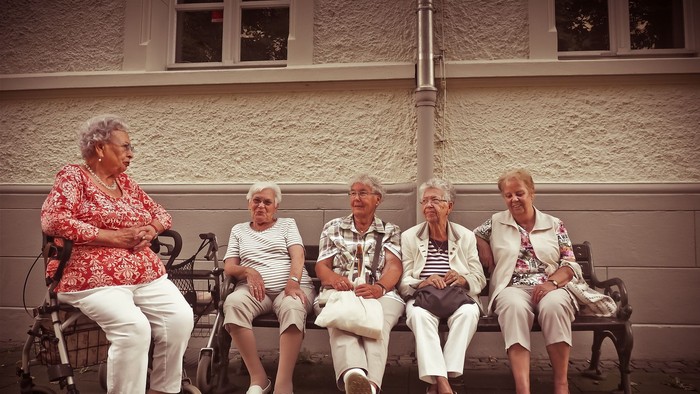 Fünf ältere Frauen sitzen auf einer Bank vor einem Gebäude