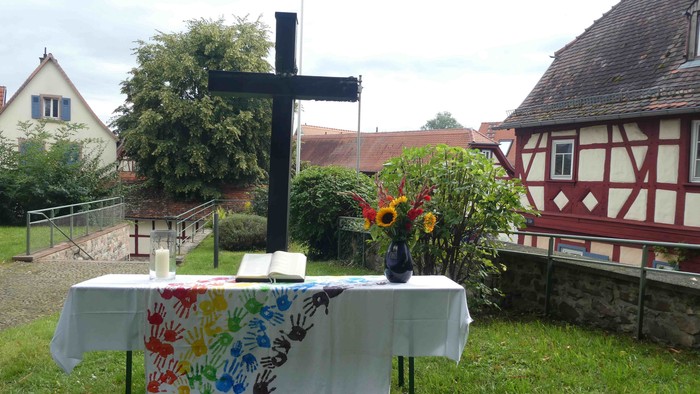Ein Tisch mit Blumen und Kreuz im Garten, umgeben von Häusern