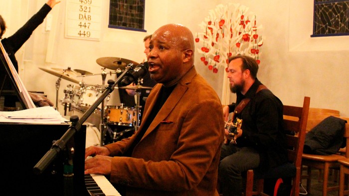 En mand spiller piano og synger i et lille café.