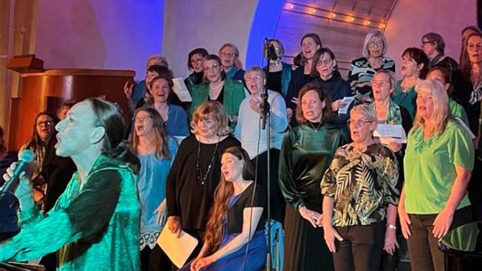 En stor gruppe af mennesker står sammen og synger i en kirke.
