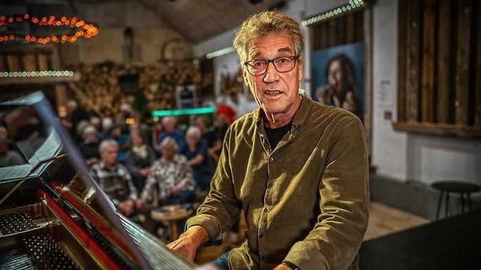 En mand spiller klaver i et hyggeligt lokale fyldt med opmærksomme, ældre tilskuere.