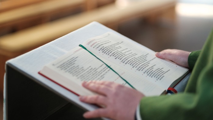 Priester im grünen Gewand steht am Ambo und verkündet das Tagesevangelium.