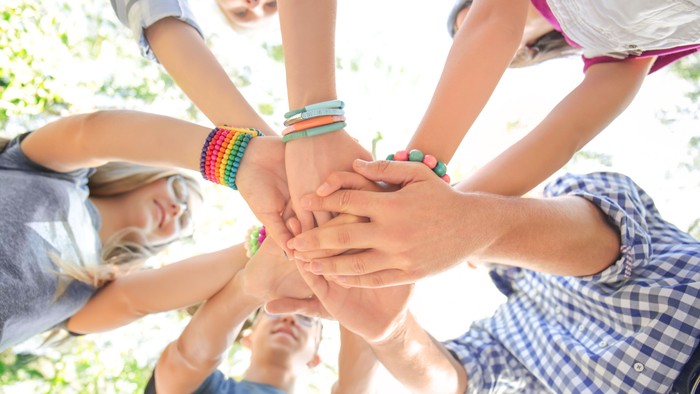Eine Gruppe von Menschen, die sich im Freien im Kreis die Hände reichen und Einheit und Teamwork symbolisieren.