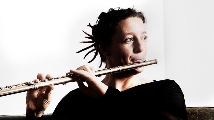 En musiker spiller fløjte, mens vedkommende sidder afslappet i en uformel stilling.