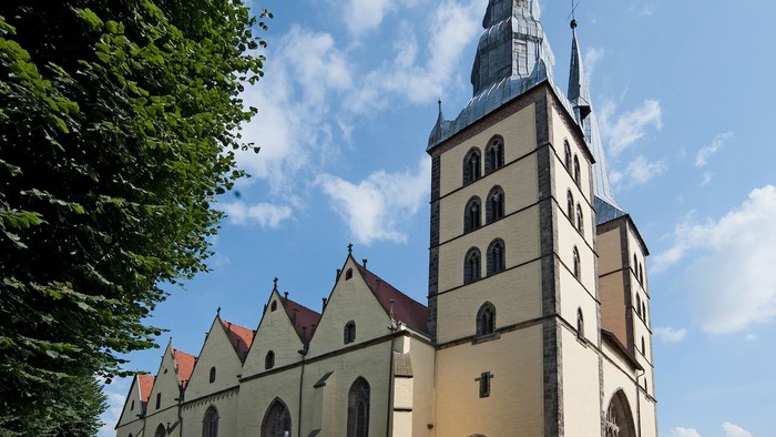 Große Kirche mit hohem Turm und spitzen Dachformen vor blauem Himmel