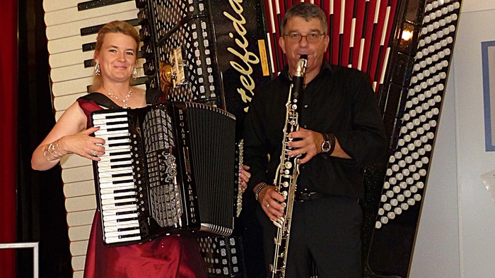 Musiker, die Akkordeon und Klarinette in formeller Kleidung spielen und gemeinsam posieren.