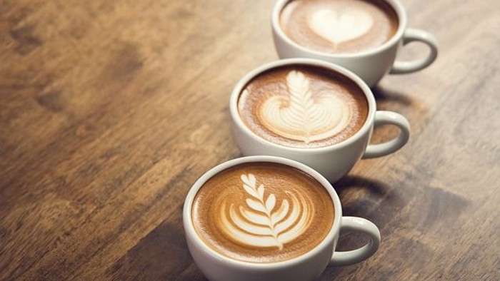 Tre espresso-tassen med latte-kunst på træbord