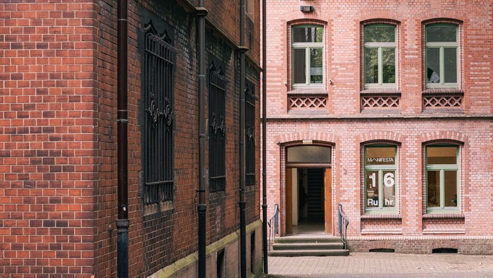 Historisches Backsteingebäude mit Bogenfenstern und nummeriertem Eingang, verziert mit dekorativem Schmiedeeisen und einem kleinen Innenhof.