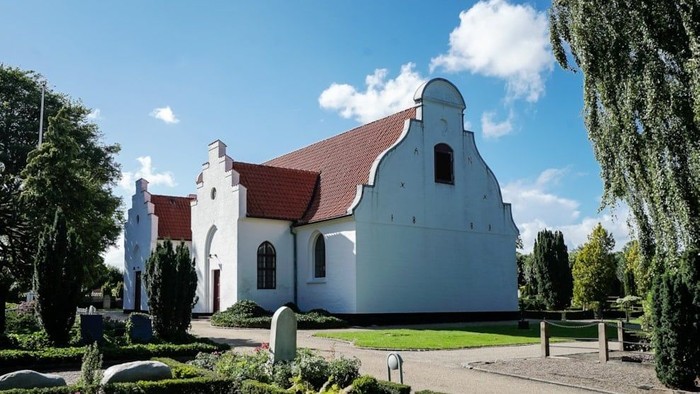 Hvid kirke med rødt tag, omgivet af grønt under blå himmel