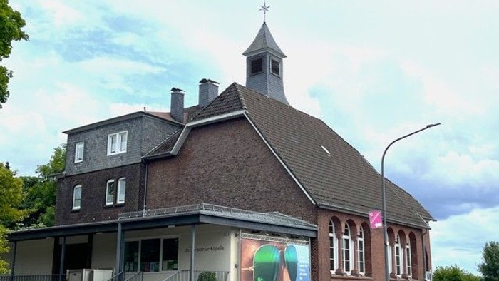 Eine malerische Backsteinkirche mit einem kleinen Turm und einem bunten Wandgemälde an der Außenwand neben einer Straße.