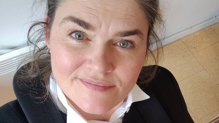 En person iført en sort dobbeltradet blazer med en hvid skjorte, der smiler til kameraet.