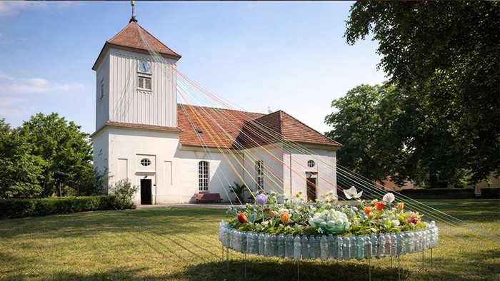 Bunte Schnüren ziehen sich von Blumen-Installation am Boden bis zum Kirchturm Altstaaken.