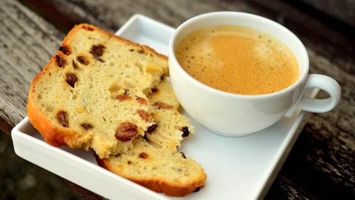 Ein Stück Früchtebrot, serviert mit einer dampfenden Tasse Kaffee auf einem Tablett.