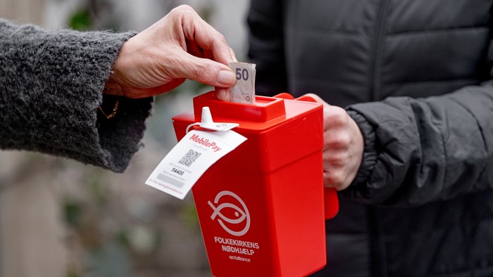 En person lægger en 50-krones seddel i en rød indsamlingsskål.