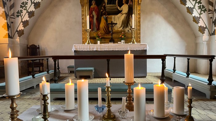 En altertavle med religiøse billeder i en kirke, omgivet af lysede lygter og candelabre.