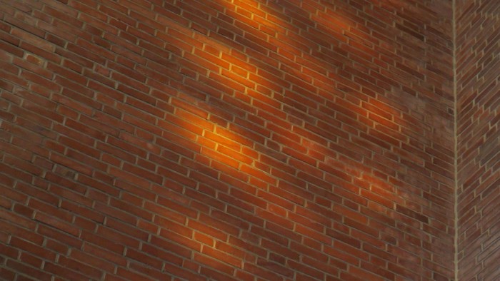 Warmes Licht wirft leuchtende Muster auf eine strukturierte Backsteinmauer.