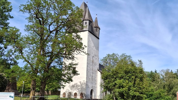 Historischer Steinkirchturm, umgeben von üppigem Grün unter einem klaren blauen Himmel.