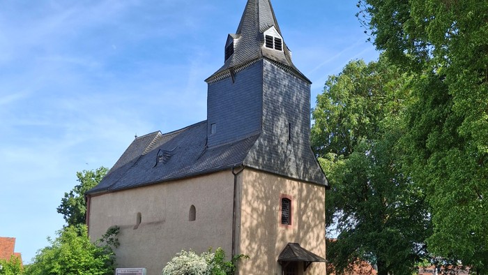 Historische Steinkirche mit hohem Glockenturm, umgeben von üppigem Grün und einem Kopfsteinpflasterweg.