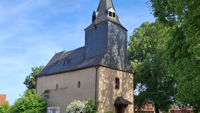 Historische Steinkirche mit hohem Glockenturm, umgeben von üppigem Grün und einem Kopfsteinpflasterweg.