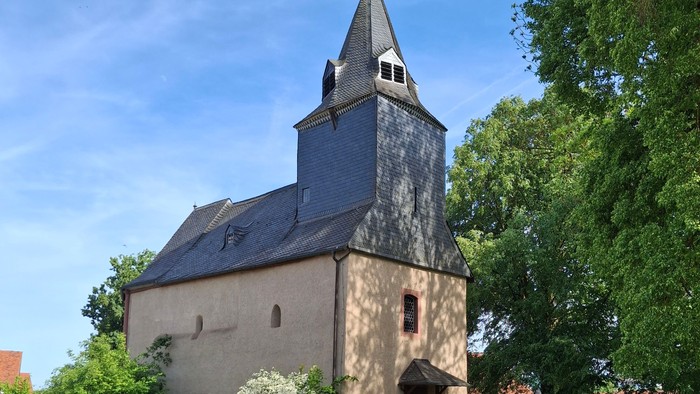 Historische Steinkirche mit hohem Glockenturm, umgeben von üppigem Grün und einem Kopfsteinpflasterweg.