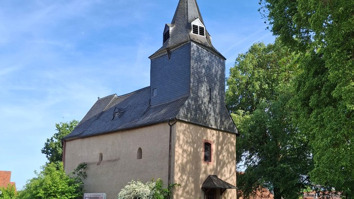 Historische Steinkirche mit hohem Glockenturm, umgeben von üppigem Grün und einem Kopfsteinpflasterweg.
