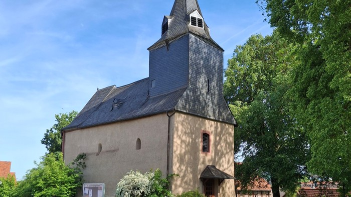 Historische Steinkirche mit hohem Glockenturm, umgeben von üppigem Grün und einem Kopfsteinpflasterweg.