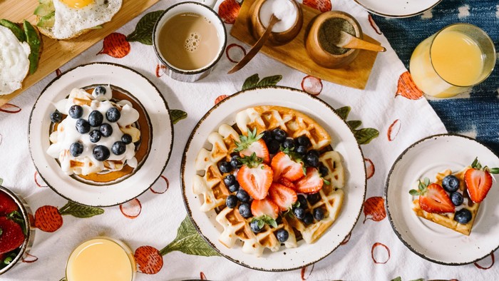 Ein Frühstücksbuffet mit Waffeln, Obst, Eiern und Saften auf einem Tisch