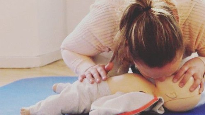 En kvinde udfører first aid på et barn på en blå matte.