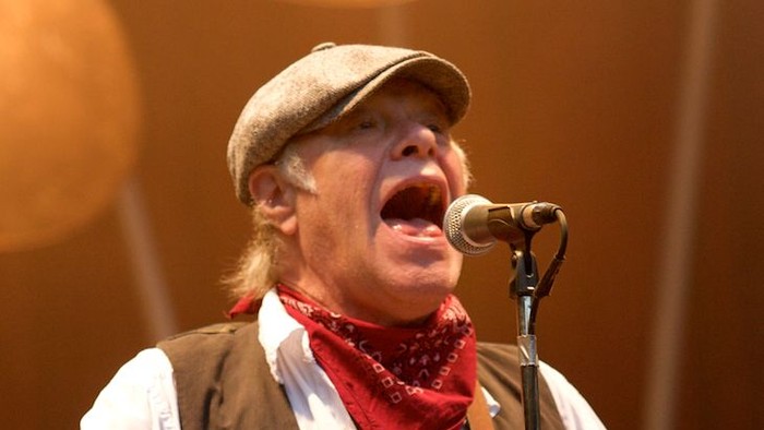 En passioneret musiker, der synger i en mikrofon, mens han spiller på en basguitar på scenen.