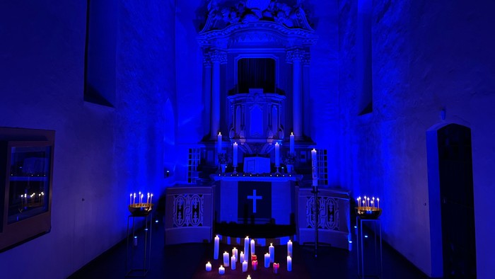 Kirchlicher Raum mit blauer Beleuchtung und zahlreichen Kerzen
