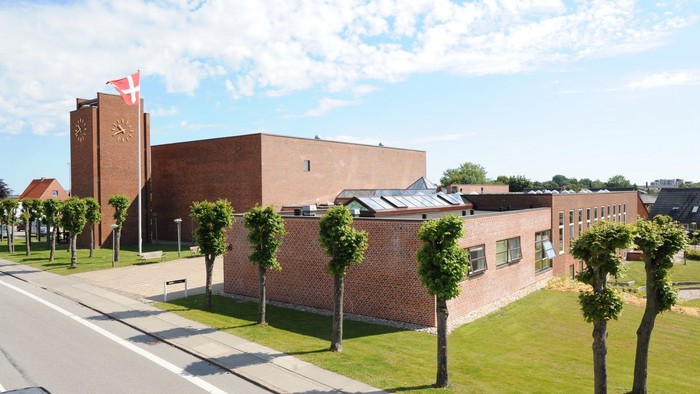Et rødt murstensbygning med klokketårn og canadisk flag ved en vej