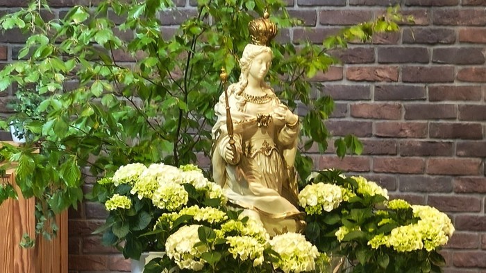 Eleganter Altartisch mit einer Statue, Blumengestecken, Kerzen und einer drapierten Tischdecke.