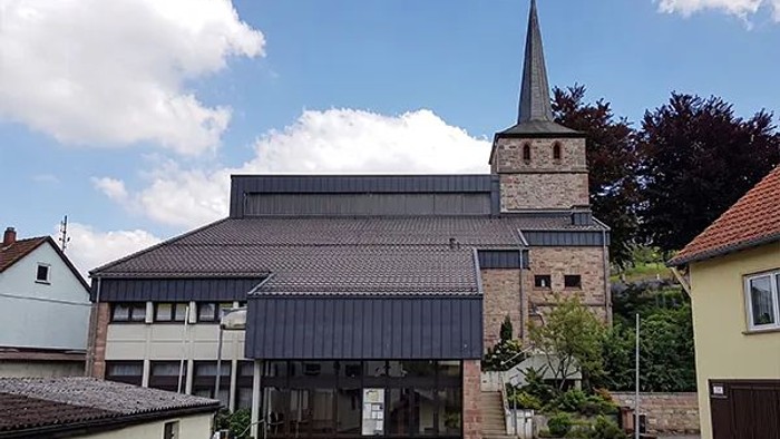Moderne Kirchengebäude neben einer älteren Steinkirche mit hohem Kirchturm.