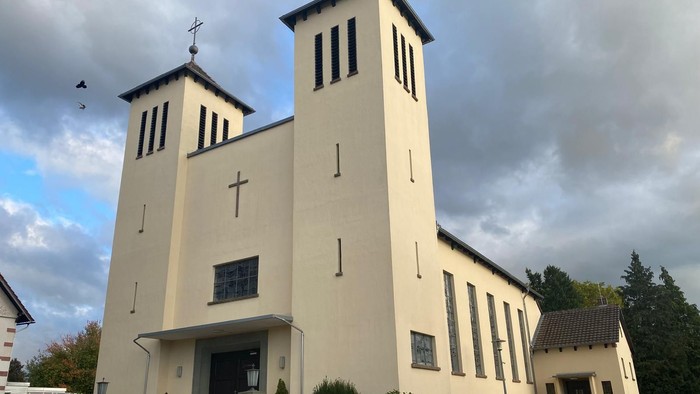 Moderne Kirche mit Zwillingstürmen, hellem Äußeren und gestaltetem Eingangsbereich unter bewölktem Himmel.