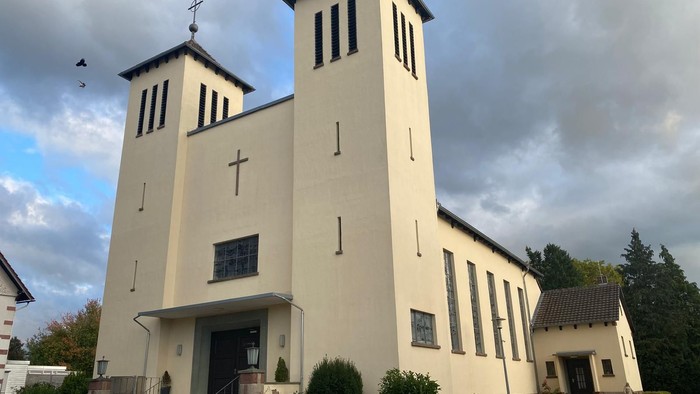 Moderne Kirche mit Zwillingstürmen, hellem Äußeren und gestaltetem Eingangsbereich unter bewölktem Himmel.