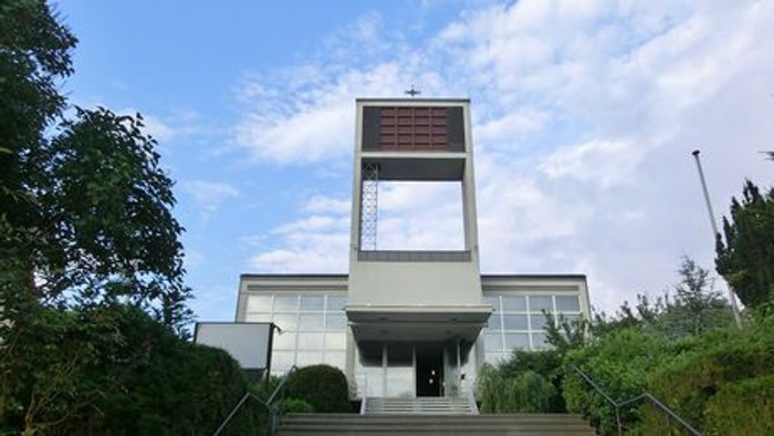 Moderne Kirche mit hohem, rechteckigem Glockenturm und breiter Treppe zum Eingang.