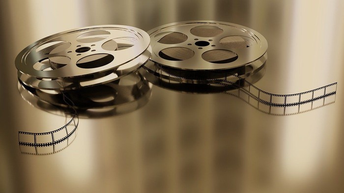 Zwei alte Filmrollen mit freiliegenden Schwarz-Weiß-Filmstreifen auf einer reflektierenden Oberfläche.
