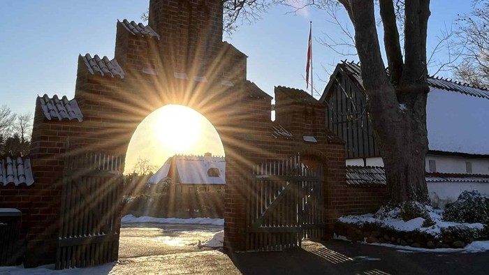 Solskin kommer ind gennem porten til kirkepladsen ved Ishøj Kirke på en vinterdag med sne