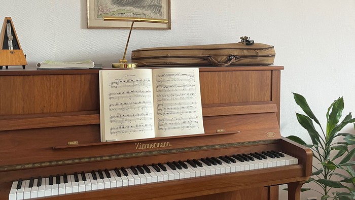 Elegantes Holzklavier mit Notenblättern, gerahmten Kunstwerken und einer kleinen Topfpflanze in der Nähe.