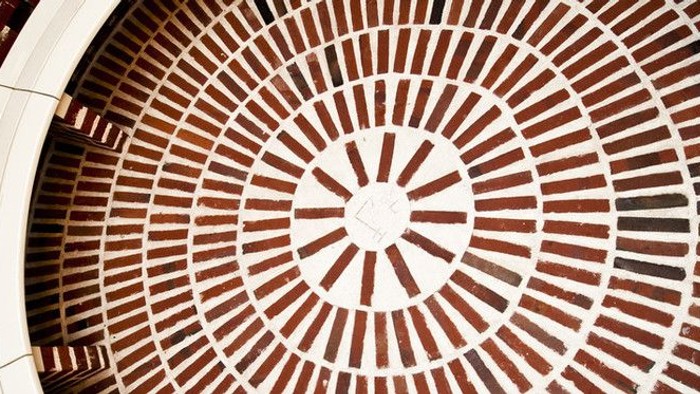 Indviklet cirkulært mosaikgulv med koncentriske geometriske flise-mønstre i jordfarver.