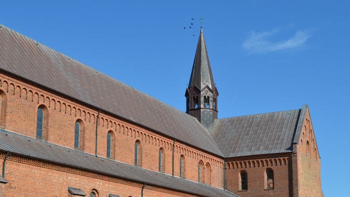 Historisk murstenskirke med højt spir og buede vinduer under klar blå himmel.