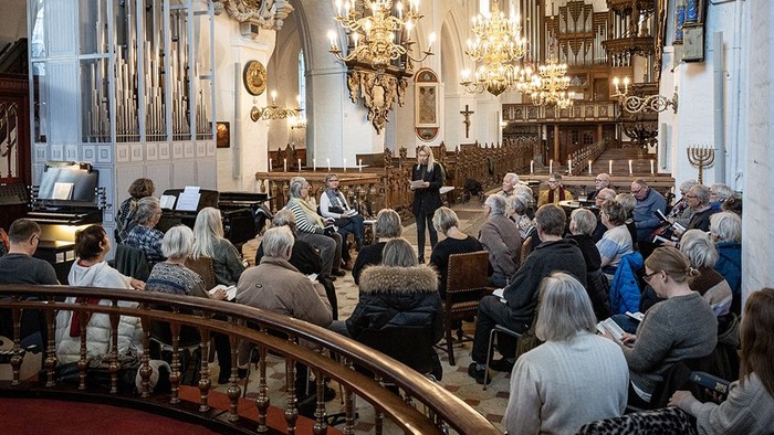 En menighed samles i en stor kirke til en gudstjeneste og lytter opmærksomt til taleren forrest.