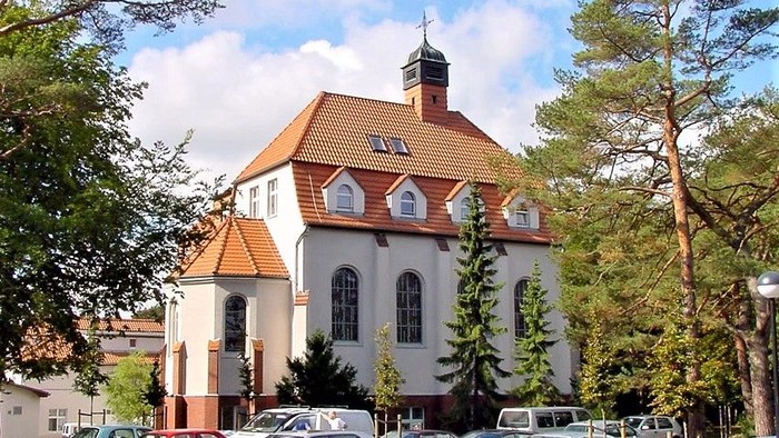 Ein weißes Gebäude mit rotem Dach und Turm, umgeben von Bäumen und Autos.